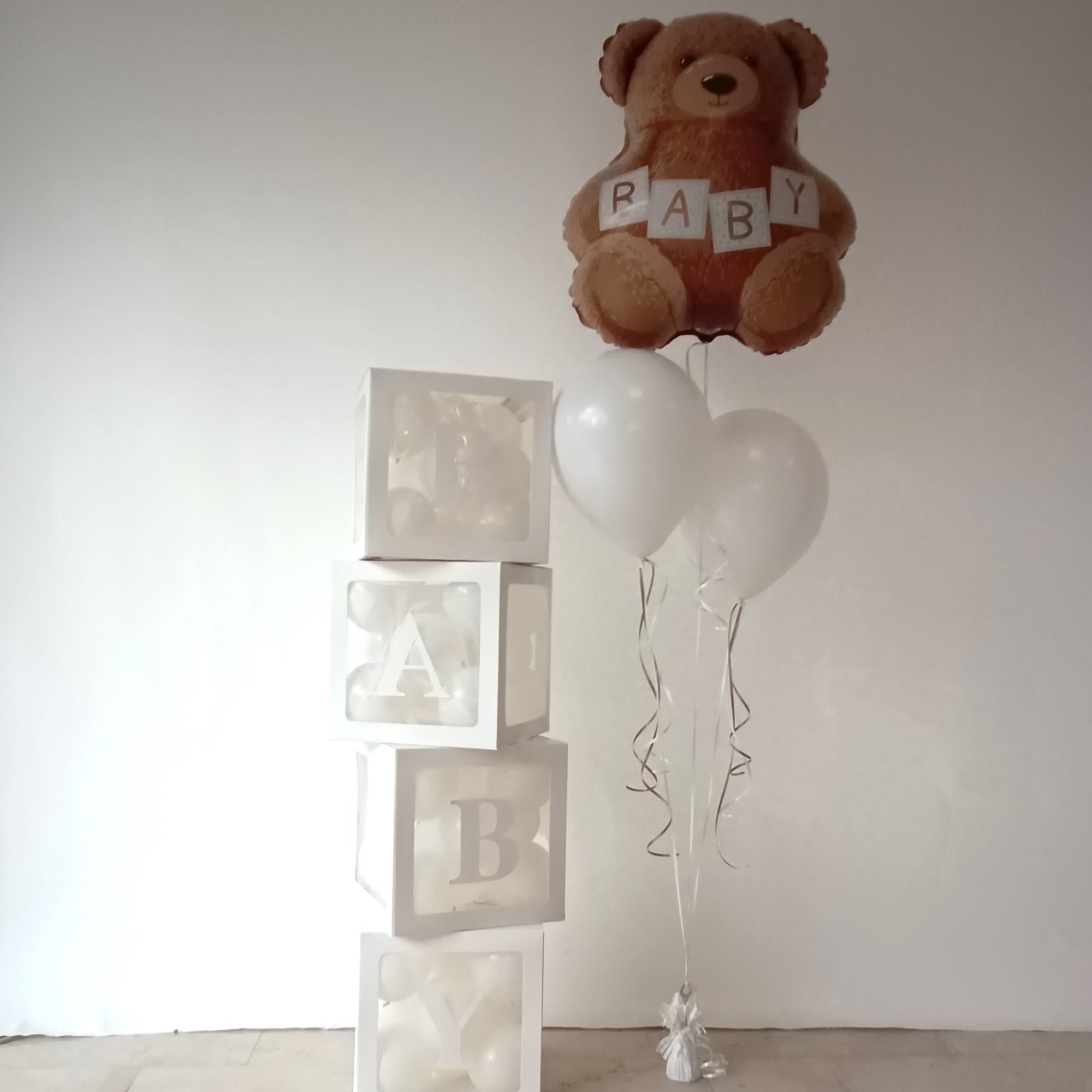 Ballondekoration mit schwebendem Folienballon in Bärenform mit BABY-Aufdruck, zwei weißen Heliumballons und vier weißen transparenten Baby-Boxen mit kleinen Ballons gefüllt