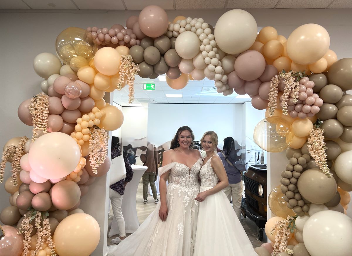 Romantischer Ballonbogen in Nude- und Cremetönen mit Glaskugeln und Trockenblumen, Brautpaar im Vordergrund