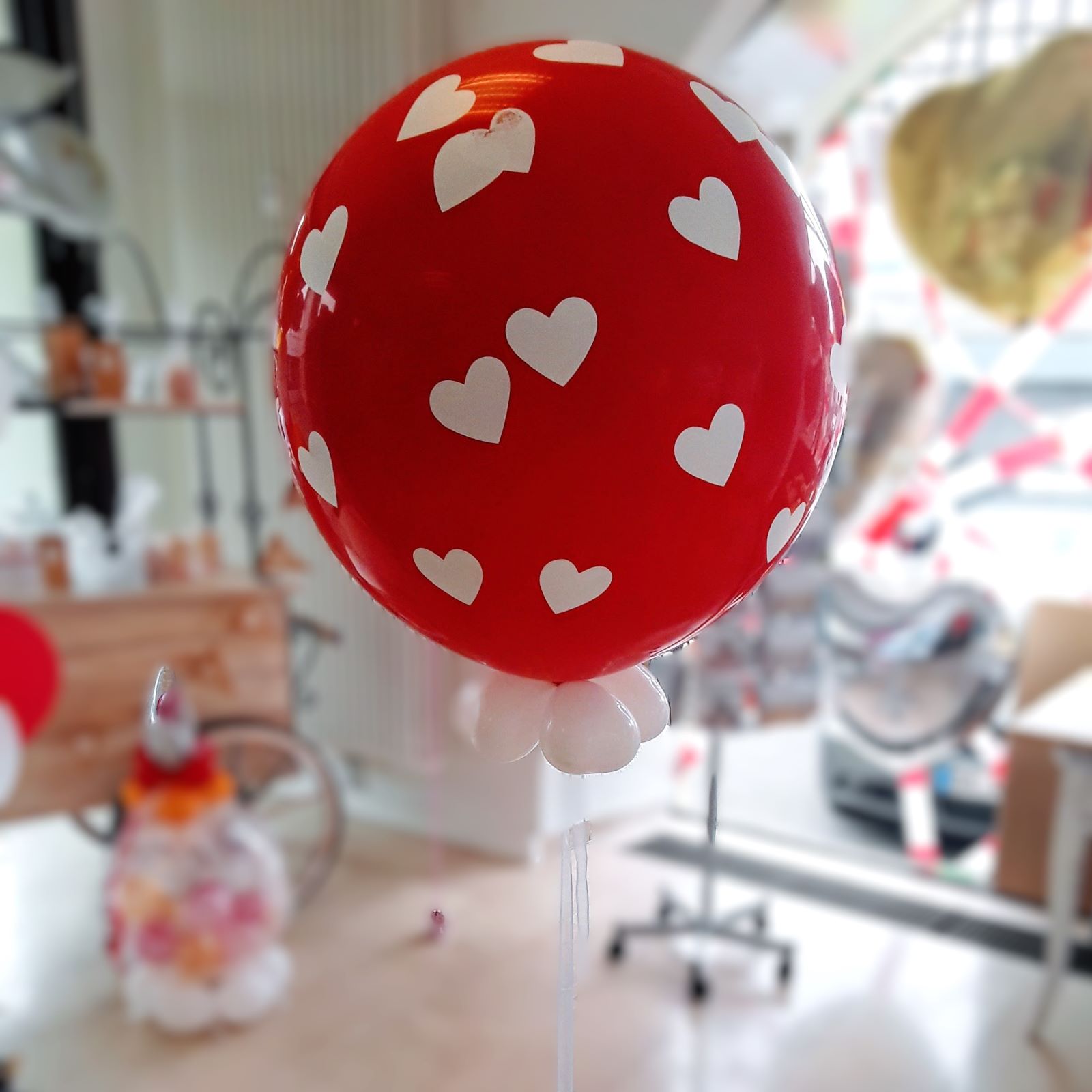 Großer roter Latexballon (ca. 80 cm) mit weißen Herzaufdrucken, gefüllt mit 30 kleinen Innenballons in Wunschfarben, gebunden an dekoratives Ballonband, heliumgefüllt