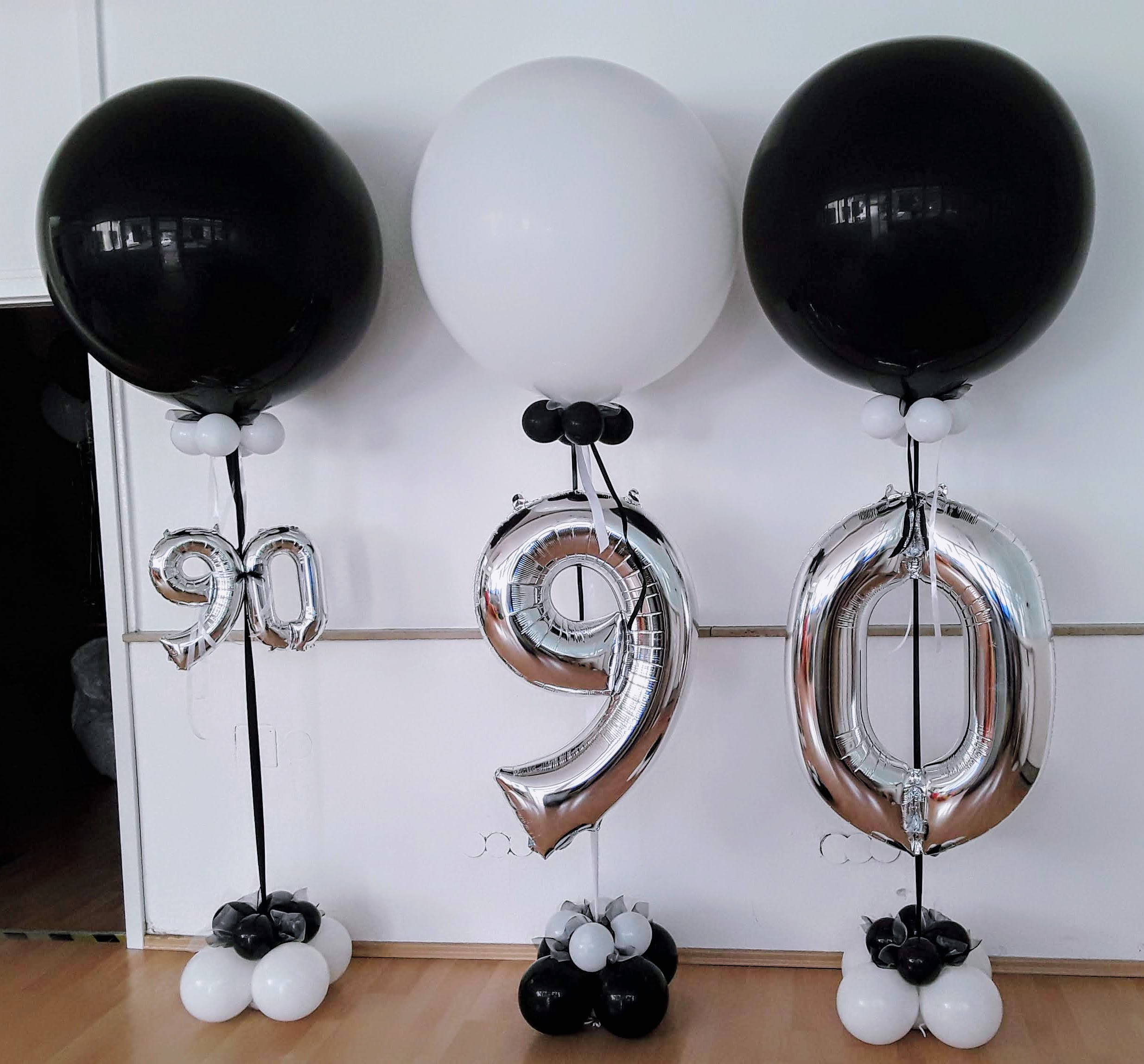 Große Zahlenballons 9 und 0 in Schwarz, Weiß und Silber, auf einem stabilen Ständer arrangiert.