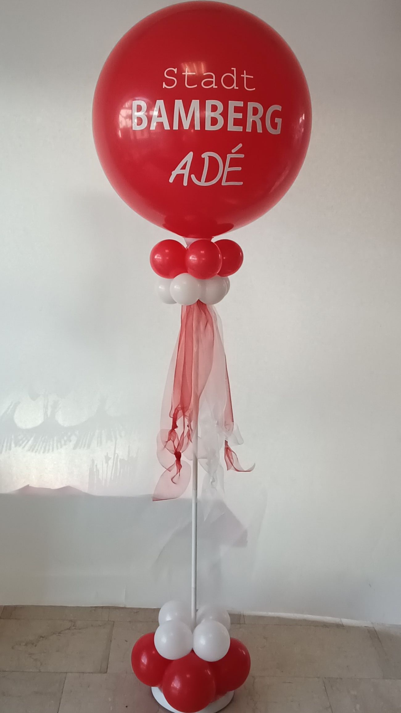 Großer roter Ballon mit weißem Aufdruck 'Stadt Bamberg Adé', dekoriert mit weißen und roten Ballons am Ständer und rotem Chiffonband.-2