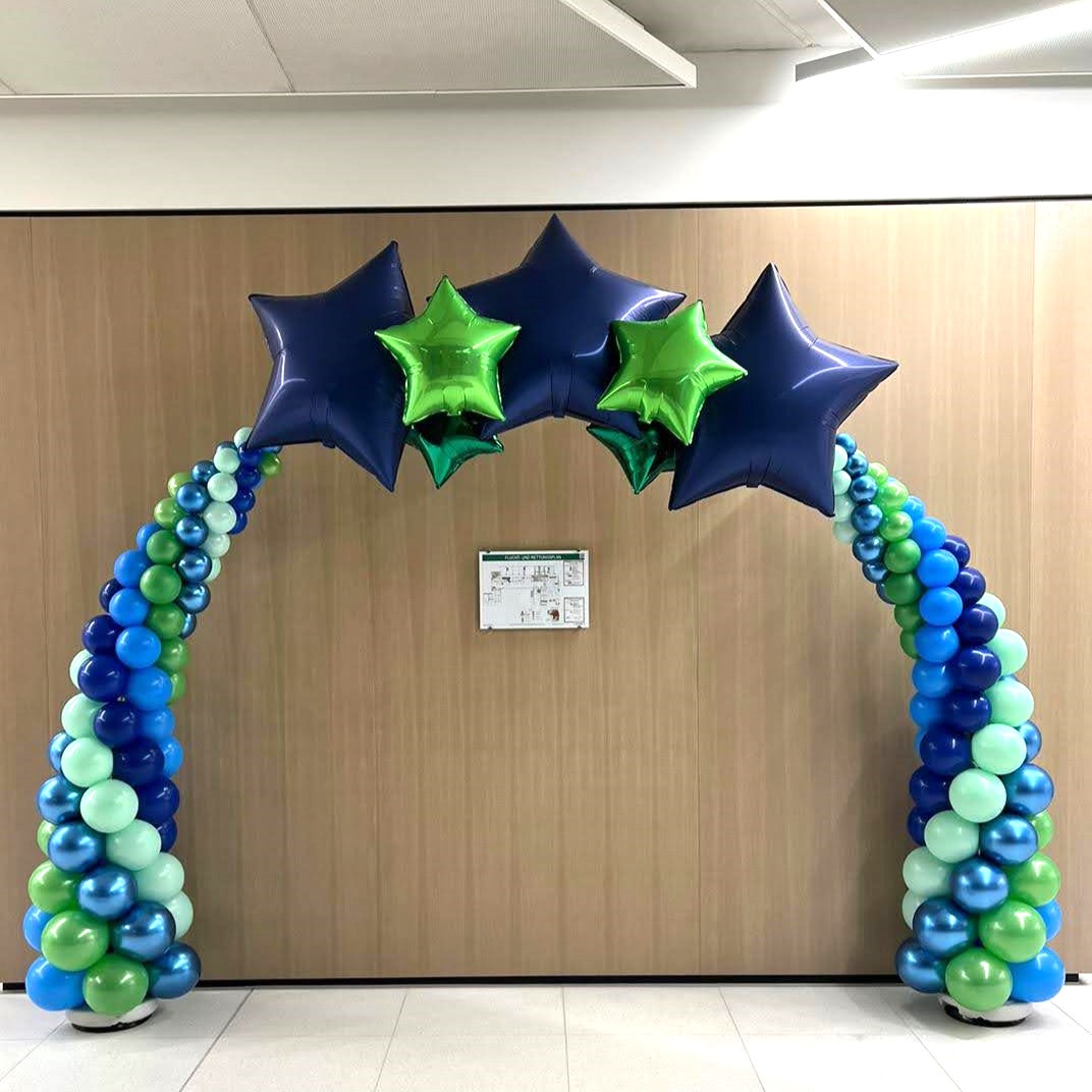 Ballonbogen aus blauen, grünen und mintfarbenen Latex- und Metallic-Ballons mit fünf Stern-Folienballons in Blau und Grün vor einer Innenwand